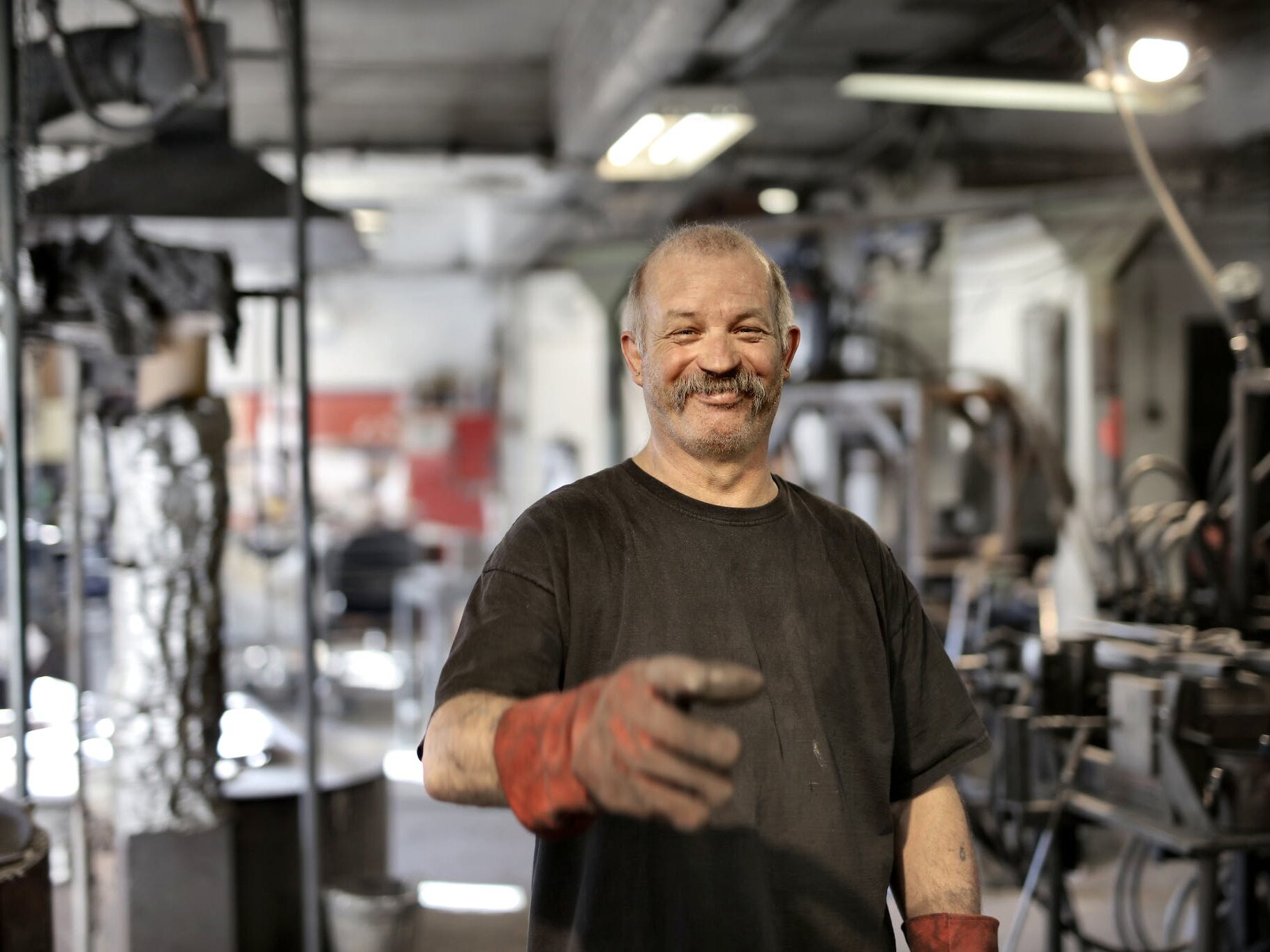 Cheerful senior white hair craftsman in heavy duty gloves laughing in workshop while looking at camera